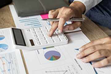 Financial scholars are pressing white calculators to calculate numbers on financial documents to verify the accuracy of company financial data line and pie chart documents. Finance concept.