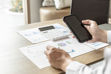 Businessman talking to a partner in a smartphone app, he is checking the accuracy of company financial data, financial status documents in line and pie charts. Finance concept.