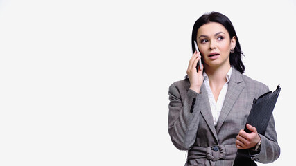 Brunette businesswoman in jacket holding clipboard and talking on smartphone isolated on white.