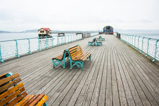 Few wooden benches on a wooden pier in front of new and old lifeboat station. The Mumbles, Wales.