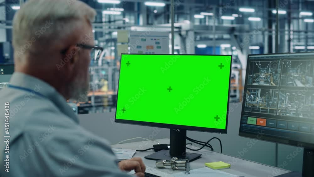 Poster Car Factory Monitoring Office: Male Chief Automotive Engineer Sitting at the Desk Working on Green Screen Chroma Key Computer. Automated Robot Arm Assembly Line Manufacturing Vehicles