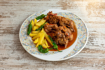 Typical Spanish stew of oxtail with garnish of homemade chips with fried padron peppers on wooden table