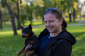Young woman enjoys companionship with her beloved pinscher dog in a city park. Selective focus with...