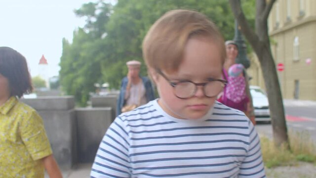 He uses glasses to improve his vision. Spending free time to walk the daily rate. Down syndrome boy moves with his family around city. 