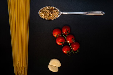 Composition of spaghetti, spoons with spices, cherry tomatoes and garlic. Food photo. Cooking. Kitchen