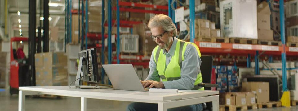 Warehouse worker or manager working on his laptop computer while sitting at a desk.