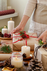 Zero waste, eco friendly christmas presents wrap concept. Young woman pack gifts in recyclable craft paper, decorate with cone, dry orange, pine branch, ribbons. Holiday atmosphere, festive mood.