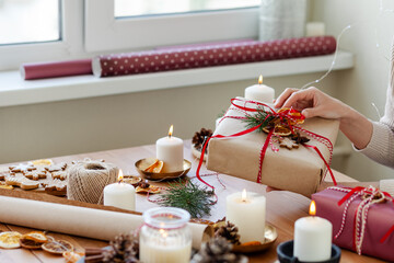 Zero waste, eco friendly christmas presents wrap concept. Young woman pack gifts in recyclable craft paper, decorate with cone, dry orange, pine branch, ribbons. Holiday atmosphere, festive mood.