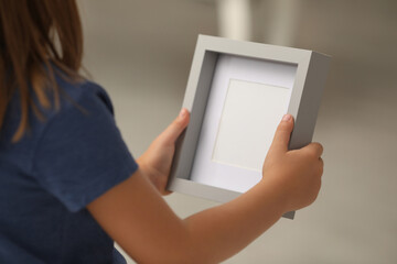 Little girl holding empty photo frame on blurred background, closeup