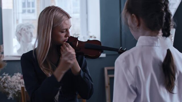 Young woman teacher tuning the violin in front of her little girl student