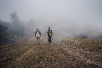 Fototapeta premium Two man friends with backpack hiking together in autumn fog nature. Male backpacker relax and enjoy walking on mountain trail. Healthy outdoor lifestyle holiday vacation concept.