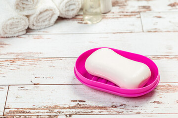 Fototapeta na wymiar soap on pink plastic soap dish with towels on white wooden table in bathroom