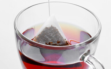 Black tea in a pyramid bag is brewed in hot water in a transparent cup. View from above. White background. Macro. Selective focusing