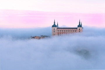 Aerial view of the ancient castle Alcazar of Toledo through the fog in colorful sunrise, Toledo, Spain.