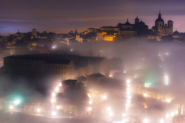  Aerial view of the old part of the city with emblematic buildings such as the courts, with the street lamps visible in the fog in the mist on a winter night with stars, Toledo, World Heritage City, S - obrazy, fototapety, plakaty