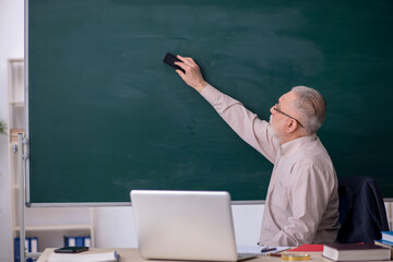 Old male teacher in front of blackboard