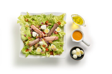 Top view of fresh salad of roasted beef, ham and quail eggs, with condiments aside, isolated