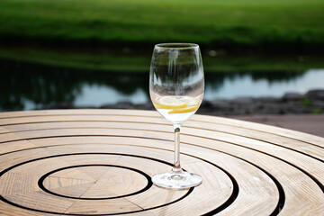Fototapeta na wymiar Refreshing glass of water with lemon on round wooden table on a sunny summer day outdoor