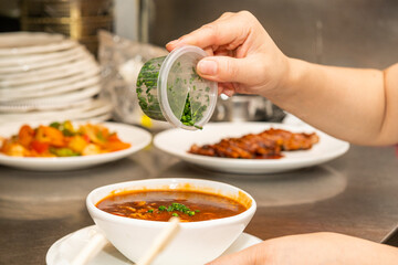 Cook's hands pouring pre-cut chives into a bowl of hot ramen.
