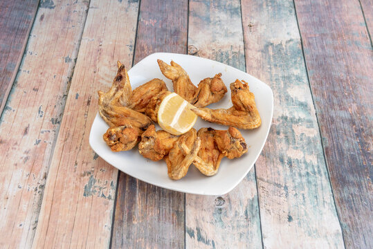 Portion Of Fried Chicken Wings With A Lemon Wedge To Garnish Served In A Spanish Tapas Restaurant On A White Plate