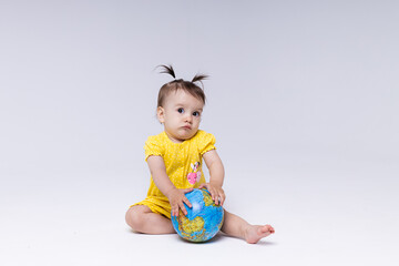 A European girl in yellow clothes sits on a white background and holds a globe in her hands. A girl with tails on a white background is surprised.