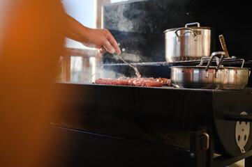 Caucasian male's hand grilling pork meat, known as cevapi - Balkans cuisine