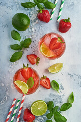 Two glasses of punch and fresh ingredients for making lemonade, infused detox water or cocktail. Strawberries, lime, mint, basil, ice cubes and shaker on grey stone or concrete background. Top view.