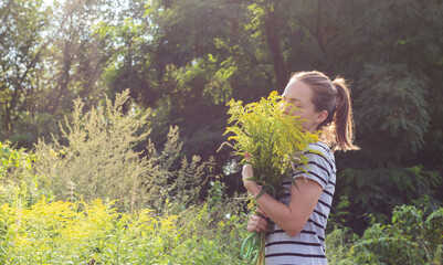Middle-aged adult Russian woman outdoors holds a bouquet of yellow wildflowers in her hands,...