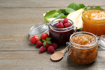 Jars with different jams and fresh fruits on wooden table. Space for text