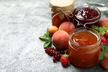 Jars with different jams and fresh fruits on grey table. Space for text