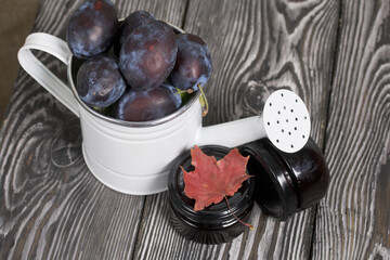 Large plums in a metal watering can. On pine boards. Nearby is a jar of jam. Harvest plums.