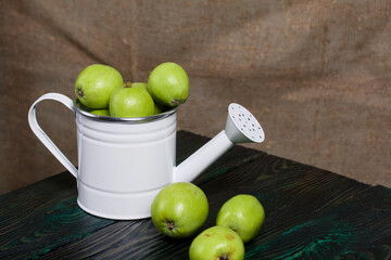Green apples in a metal watering can.  On pine boards.  On a linen background.  Harvest apples.
