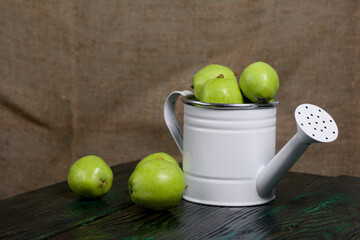 Green apples in a metal watering can.  On pine boards.  On a linen background.  Harvest apples.