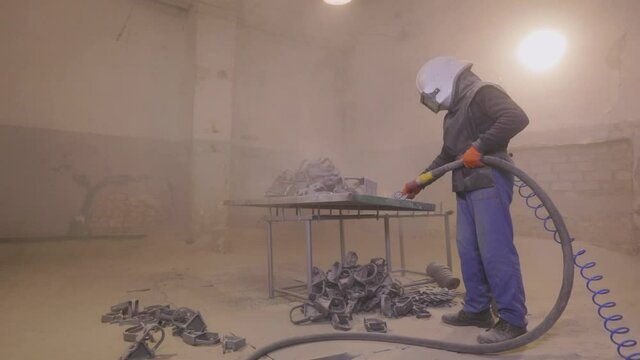 The man is sandblasting the detail. Sandblast metal parts. Sandblasting gun