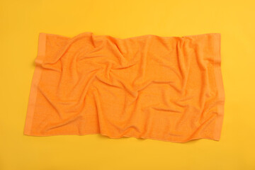 Crumpled orange beach towel on yellow background, top view
