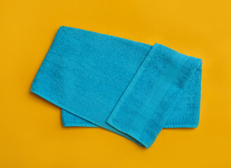 Folded light blue beach towel on yellow background, top view