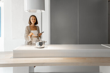 Young stylish woman cooking on induction hob at modern kitchen. Concept of smart technologies of...
