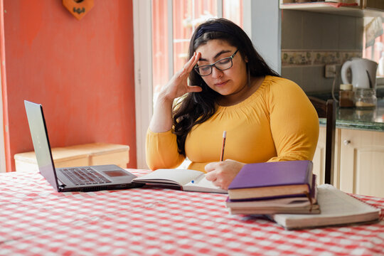 Concentrated Hispanic Young Woman Studying Online - Tired And Distressed Student With Hand On Head While Studying At Home - Woman With A Lot Of Work From Home