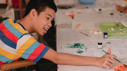 Handicapped teenager boy on wheelchair with happy face doing art work with friends, Lifestyle of...