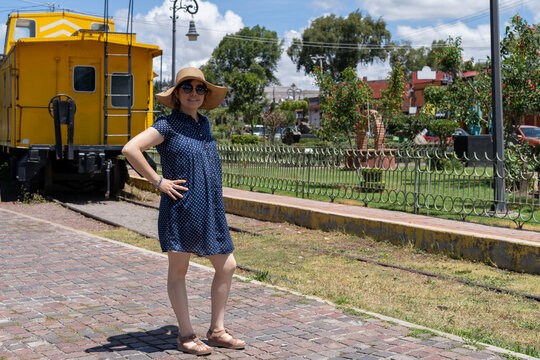 vag&oacute;n tren mujer modelando sombrero vestido azul c&eacute;sped parque amarillo arboles 