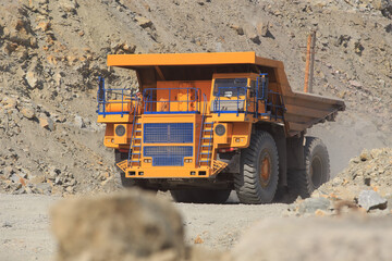 Large yellow mining dump truck on the road on a sunny day. Large-sized equipment for the transportation of rock mass in an ore quarry.