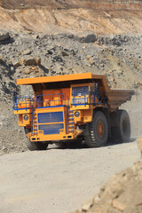 Large yellow mining dump truck on the road on a sunny day. Large-sized equipment for the transportation of rock mass in an ore quarry.