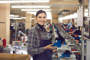 Young proud smiling female shoe designer smiling to camera holding part of new footwear. Online...