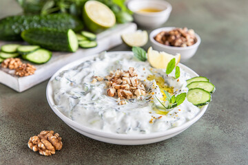 Traditional bulgarian cold summer soup tarator with ingredients on green background. Bulgarian soup with grated cucumbers, yogurt and walnuts.