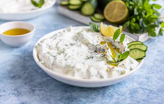 Indian or Pakistani raita sauce or dip with cucumber, yoghurt, garlic and mint, blue concrete background. Traditional Indian cuisine.