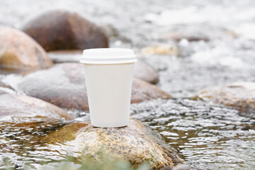 white paper coffee cup mock up 
on a rock by a mountain river