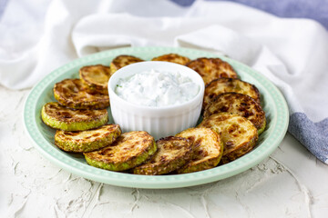 Fried slices of zucchini with sour cream sauce on plate. Fried courgettes with herb for dinner on white background