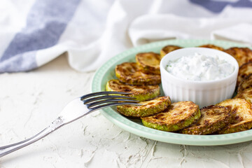 Fried slices of zucchini with sour cream sauce on plate. Fried courgettes with herb for dinner on white background