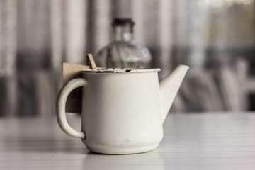 Fototapeta premium Kitchen décor, café décor. White rustic watering pot and a glass bottle with dry spicules inside, on white wooden table
