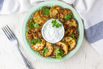 Fried slices of zucchini with sour cream sauce on plate. Fried courgettes with herb for dinner on white background